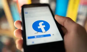 Dłoń trzyma smartfon z otwartą stroną logowania Facebook.