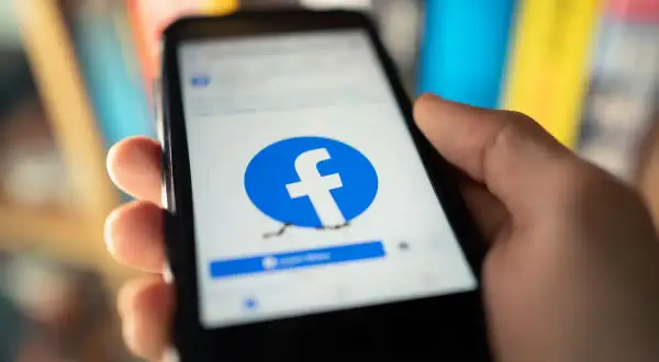Dłoń trzyma smartfon z otwartą stroną logowania Facebook.