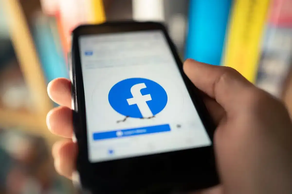 Dłoń trzyma smartfon z otwartą stroną logowania Facebook.