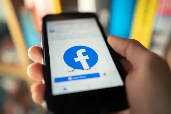 Dłoń trzyma smartfon z otwartą stroną logowania Facebook.